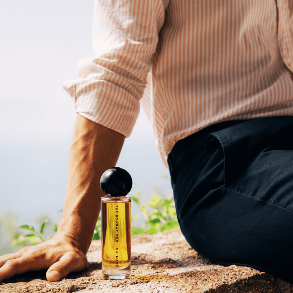 Gulmarg 60ml perfume placed beside a seated man outdoors, evoking a fresh, natural vibe inspired by Himalayan mornings.