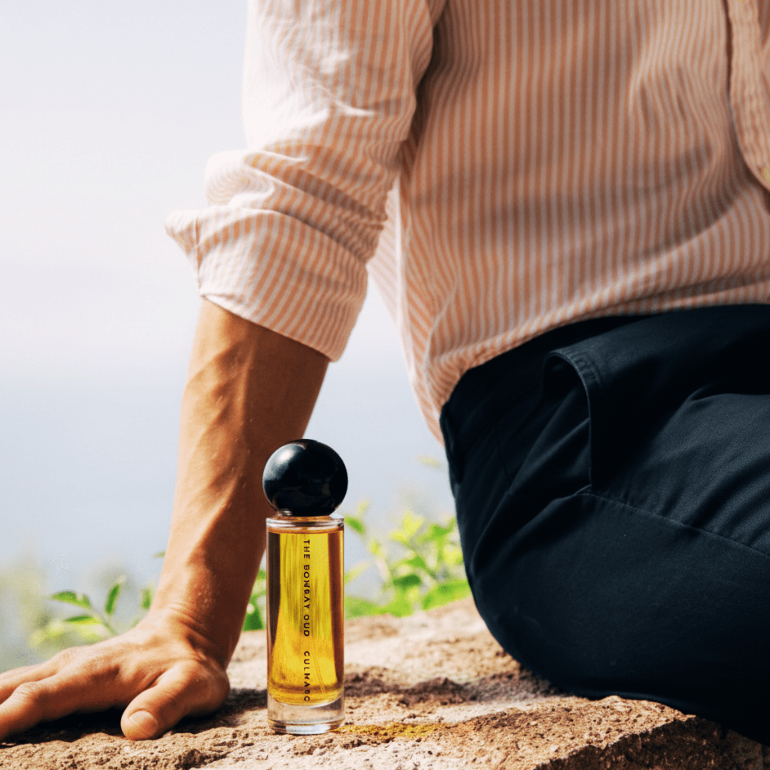 Gulmarg 60ml perfume placed beside a seated man outdoors, evoking a fresh, natural vibe inspired by Himalayan mornings.