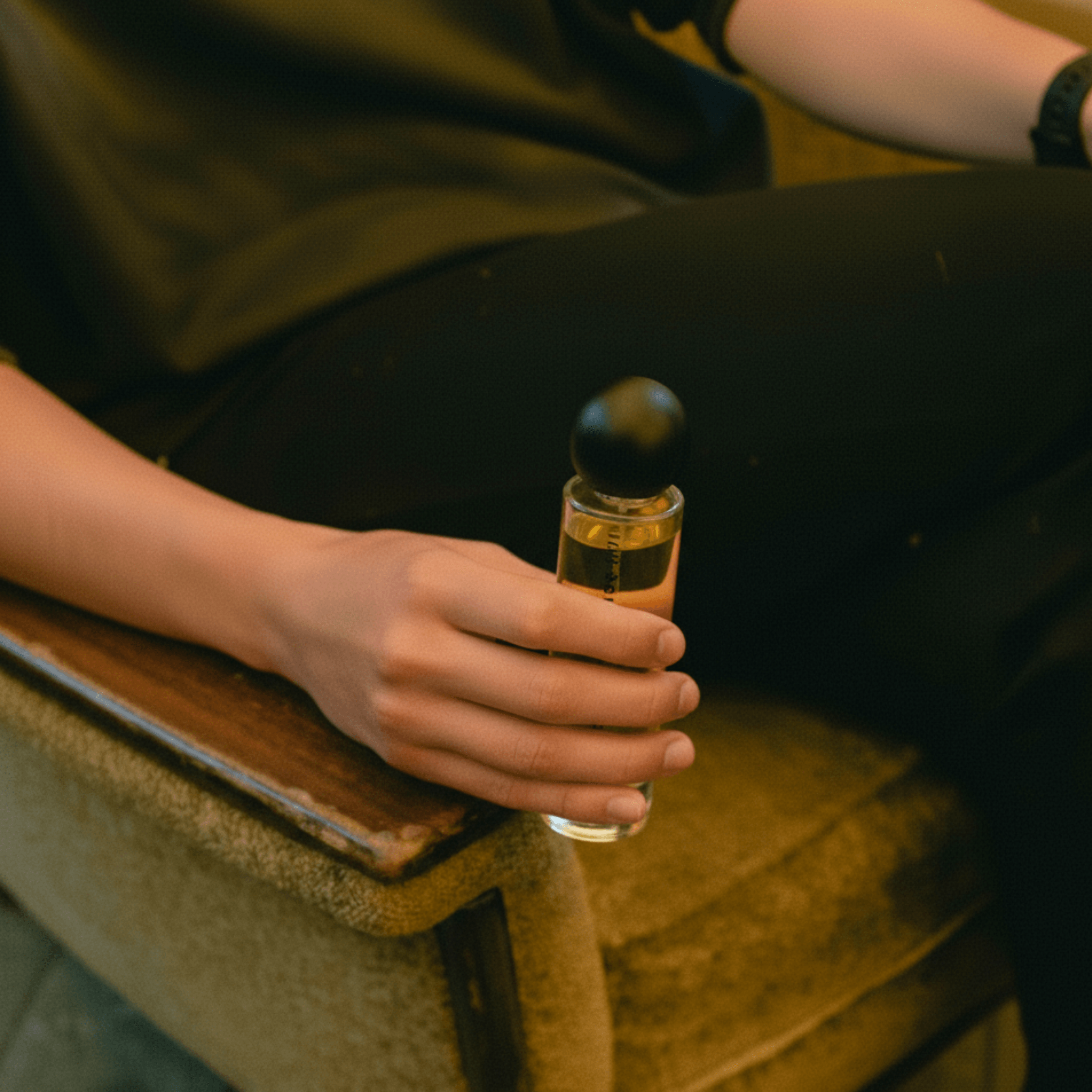 Person holding Kasol 60ml perfume bottle while seated, showcasing its sleek design and personal luxury appeal in daily use.