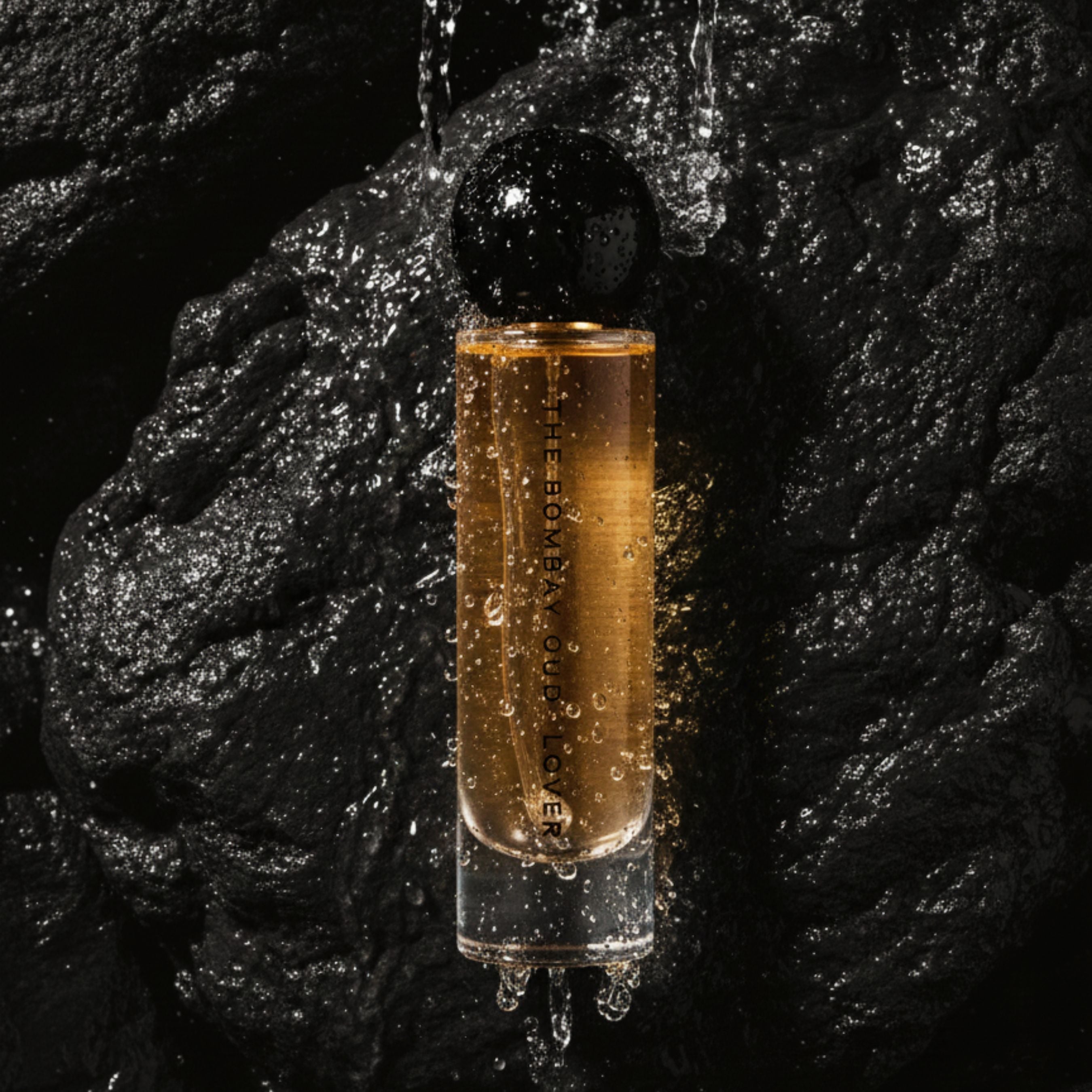 Lover 60ml eau de parfum bottle by The Bombay Oud glistening with water droplets against black stone, evoking sensual freshness.